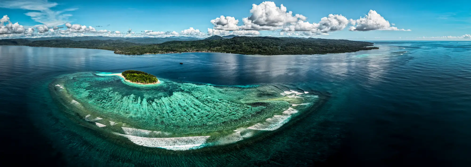 aerial view appears to show a small tropical island surrounded by an extensive coral reef in eastern Indonesia